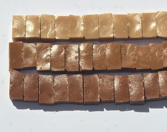May include: Three horizontal rows of rectangular, glossy, caramel-colored blocks arranged in a grid. Each row features a distinct shade of brown, ranging from a light tan in the top row to a medium brown in the middle and a deep, rich brown in the bottom row.