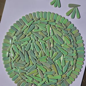 May include: A circular mosaic art piece composed of green, teardrop-shaped tiles. The tiles are arranged in a radial pattern, with a border of similar tiles. Three additional tile clusters are arranged above the circle, suggesting a stylized design.