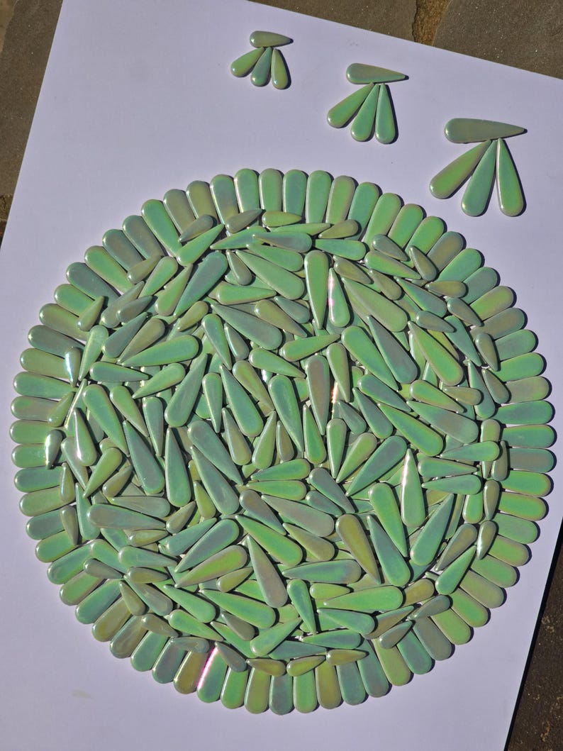 May include: A circular mosaic art piece composed of green, teardrop-shaped tiles. The tiles are arranged in a radial pattern, with a border of similar tiles. Three additional tile clusters are arranged above the circle, suggesting a stylized design.