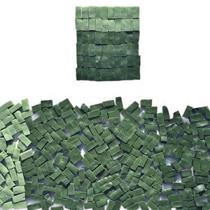 May include: An overhead shot displays a collection of small, rectangular, dark green tiles. Some tiles are arranged in a square, while others are scattered below. The tiles have a slightly textured appearance and are set against a white background.