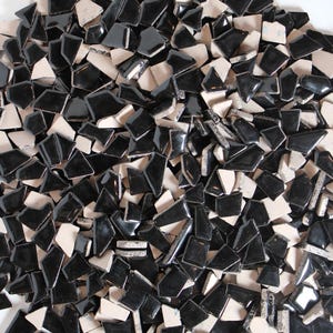 May include: A pile of black and off-white ceramic tile pieces. The pieces are various geometric shapes, with a glossy black finish on the black tiles. The off-white tiles have a matte finish. The tiles are scattered across the surface.