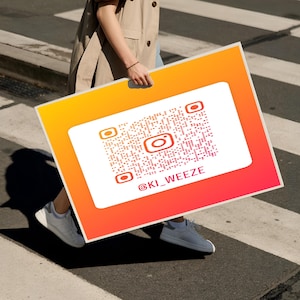 May include: A large rectangular sign with a QR code and Instagram logo, set against a gradient of orange and red. The Instagram handle @KI_WEEZE is displayed below the logo. The sign is being held by a person walking on a crosswalk.