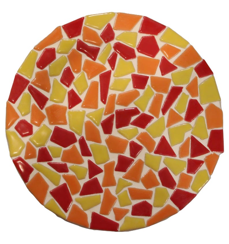 May include: A round mosaic piece with a white background and a colorful pattern. The mosaic features irregular shapes in shades of red, orange, and yellow. The piece is likely a decorative item, such as a trivet or coaster.