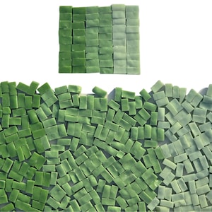 May include: A collection of small, rectangular glass mosaic tiles in various shades of green, ranging from deep forest green to pale mint. The tiles are arranged in a loose, scattered pile at the bottom and a neat, square grid at the top.