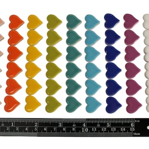 May include: A collection of colorful heart-shaped tiles in various shades of red, pink, orange, yellow, green, teal, blue, purple, white, and black. A ruler with inch measurements is at the bottom, measuring up to 6 inches.
