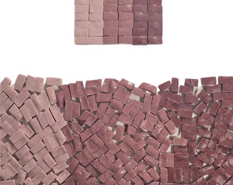 May include: A collection of small, rectangular glass mosaic tiles in three distinct shades of mauve and purple. The tiles are arranged in a neat square grid at the top and scattered in a loose, overlapping pattern across the bottom section.