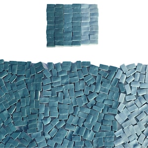 May include: An overhead shot of a collection of small, rectangular, teal-colored tiles. The tiles are arranged in a wave-like pattern at the bottom and a square at the top. The tiles have a glossy finish and are arranged against a white background.