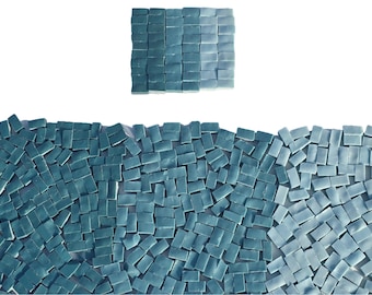 May include: An overhead shot of a collection of small, rectangular, teal-colored tiles. The tiles are arranged in a wave-like pattern at the bottom and a square at the top. The tiles have a glossy finish and are arranged against a white background.