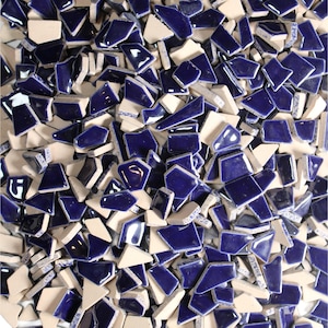 May include: A close-up shot of a pile of mosaic tiles. The tiles are a mix of shapes and sizes, with a glossy, deep blue color and a matte, off-white color. The tiles are scattered randomly, creating a textured surface.