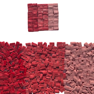 May include: An overhead shot displays a collection of small, rectangular mosaic tiles in varying shades of red and pink. The tiles are arranged in a gradient pattern, with darker reds transitioning to lighter pinks. The tiles are scattered.
