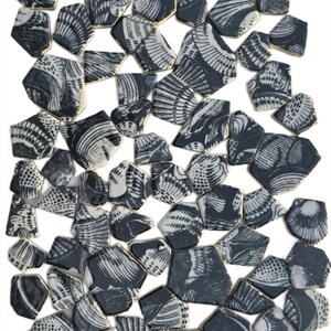 May include: A collection of irregularly shaped ceramic pieces, predominantly in shades of dark gray and white. Each piece features a detailed, stylized design, possibly depicting shells or abstract patterns. The edges are outlined in gold.