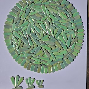 May include: A circular mosaic design composed of numerous green, teardrop-shaped tiles. The tiles are arranged in a radial pattern, with a border of similar tiles. Several smaller tile arrangements are below the main design.