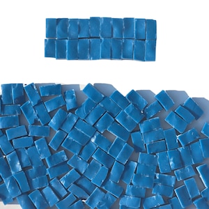 May include: An overhead shot displays a collection of small, rectangular, blue mosaic tiles. Some tiles are arranged in a neat row, while others are scattered below. The tiles have a slightly irregular shape and a matte finish.