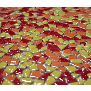 May include: A close-up view of a mosaic tile design. The mosaic is composed of irregularly shaped tiles in shades of red, orange, and yellow. The tiles are glossy and reflect light, creating a vibrant and textured surface.