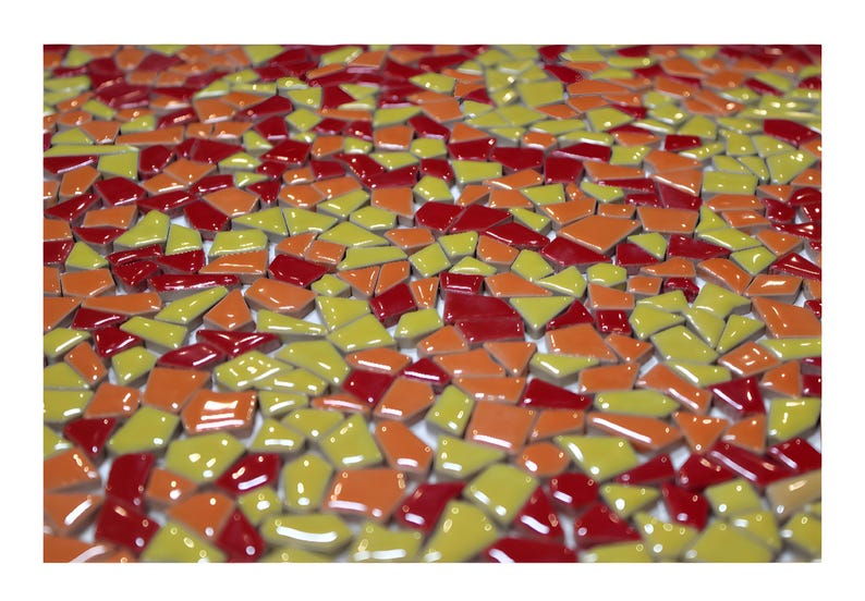 May include: A close-up view of a mosaic tile design. The mosaic is composed of irregularly shaped tiles in shades of red, orange, and yellow. The tiles are glossy and reflect light, creating a vibrant and textured surface.