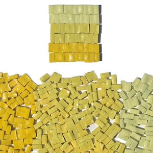 May include: A collection of small, rectangular mosaic tiles in shades of yellow and green. The tiles are arranged in a gradient pattern, with a stack of tiles at the top and a scattered arrangement below. The background is white.