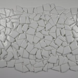 May include: An overhead shot displays a collection of irregularly shaped, white ceramic tiles. The tiles are arranged closely together, creating a mosaic-like pattern. The tiles vary in size and shape, with a glossy finish.