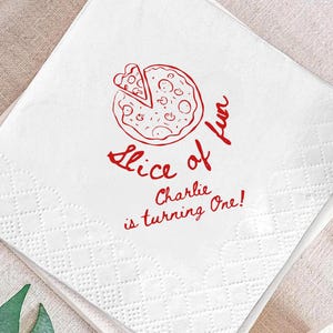 May include: A square white paper napkin featuring a red line-art illustration of a pizza with one slice removed. The text reads "Slice of fun" above the words "Charlie is turning One!" in a red script font, with a textured embossed border.