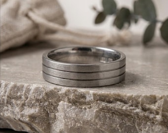 May include: A silver-coloured metal ring featuring a brushed finish and two horizontal engraved grooves circling the band. The interior of the ring shows a visible hallmark stamp, and the band has a flat profile with a consistent width throughout.