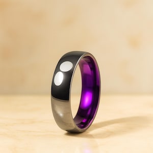 May include: A black and silver ring with a vibrant purple interior. The ring has a polished finish with two white circular accents on the black exterior. The ring is a modern piece of jewelry.