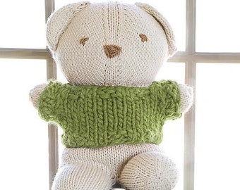 May include: A white knitted teddy bear wearing a green knitted sweater sits on a green metal toolbox. The bear has a brown nose and embroidered eyes.