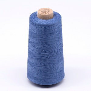 Könnte beinhalten: Eine Spule blauen Bio-Baumwollgarns mit einem Holzetikett mit der Aufschrift "I am organic - 3000 yds - 100% cotton - col 4816".
