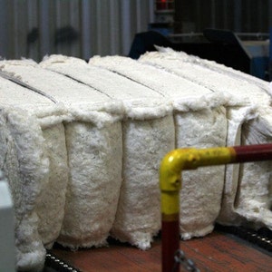 Puede incluir: Primer plano de una pila de fardos de algod&oacute;n blanco en una cinta transportadora en un entorno de f&aacute;brica. Los fardos est&aacute;n apretados y tienen una textura esponjosa.