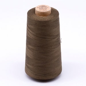 Könnte beinhalten: Eine braune Garnspule mit einem Holzkern. Das Etikett lautet "I am organic" mit Angaben zu Gewicht und Länge des Garns. Das Garn ist eng gewickelt und bildet eine konische Form. Das Garn ist etwa 2743 Meter lang.