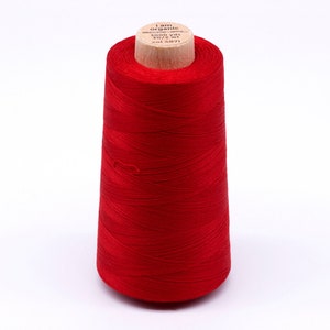 Könnte beinhalten: Eine Spule leuchtend rotes Garn. Das Garn ist um einen Holzkern gewickelt. Auf der Oberseite der Spule steht "I am organic". Das Garn hat eine einheitliche, gesättigte Farbe.