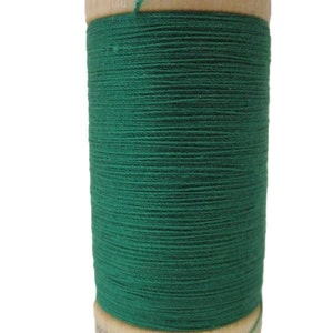 May include: A spool of green 100% organic cotton thread with a wooden label that reads "100% Organic Cotton" and "Made in E.U."