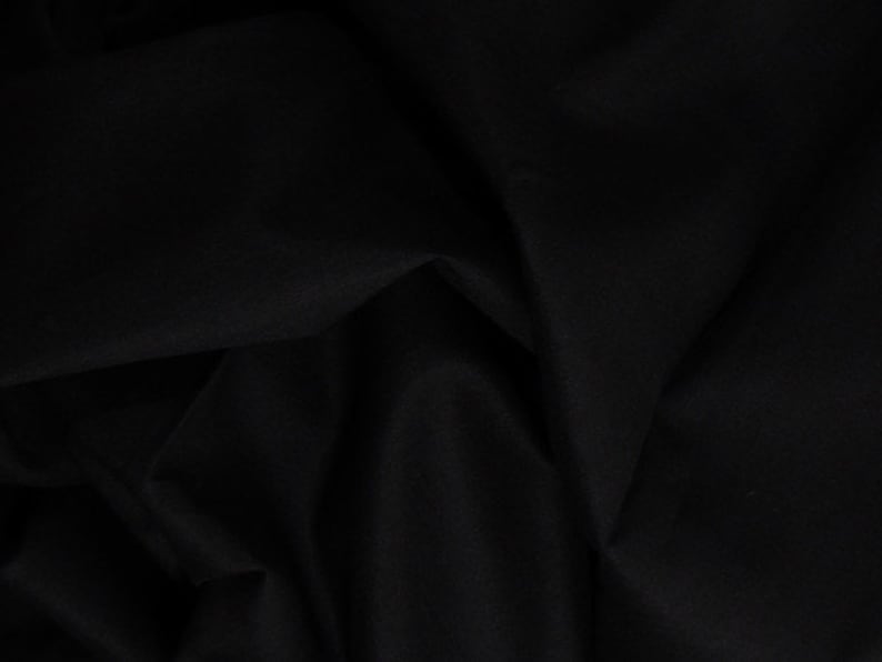 Puede incluir: Tela negra con una textura suave y lisa. La tela est&aacute; doblada y drapeada, creando una serie de pliegues y arrugas.
