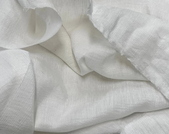 May include: White fabric with a textured, slightly wrinkled surface. The fabric is folded and draped, creating soft folds and curves.
