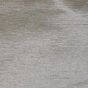 May include: Close-up of a textured fabric in a light silver-gray color. The fabric has a subtle sheen and a horizontal, linear pattern. The material appears to be soft and pliable, with slight folds and wrinkles visible across the surface.