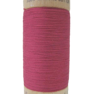 Puede incluir: Una bobina de hilo de algodón orgánico 100% en un color rosa vibrante. La bobina está hecha de madera y tiene el texto "100% ORGANIC COTTON" impreso en ella.