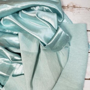 May include: A light blue satin fabric with a subtle sheen. The fabric is folded and draped, showcasing its texture and drape.