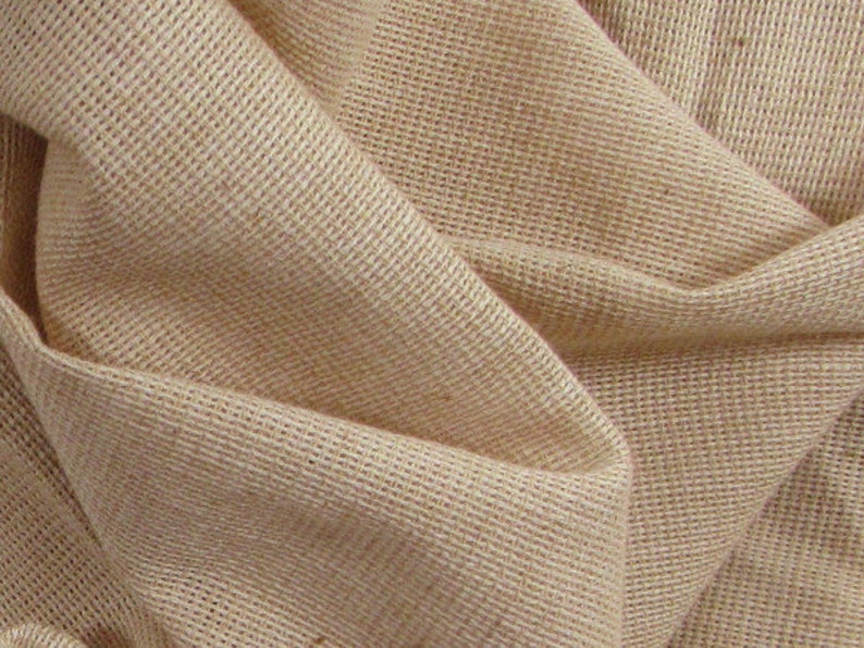 May include: A close-up of a natural brown burlap fabric with a woven texture. The fabric is folded and draped, showing the soft, pliable nature of the material.