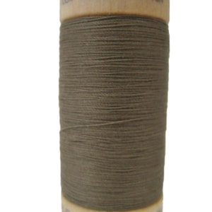 Puede incluir: Una bobina de hilo de algodón orgánico marrón con una etiqueta de madera que dice "100% algodón orgánico" y "Hecho en"