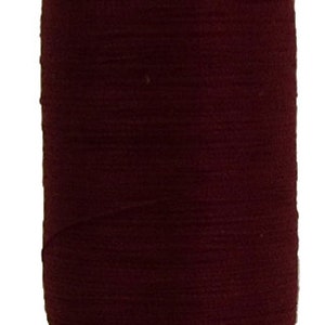 Puede incluir: Una bobina de hilo de color marrón oscuro con una bobina de madera. La bobina tiene el texto "100% ALGODÓN ORGÁNICO" y "FABRICADO EN LA UE."