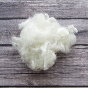 May include: A clump of white wool fibers, likely sheep's wool, on a wooden surface.