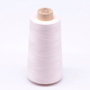 Könnte beinhalten: Eine Spule mit blassrosa Bio-Baumwollgarn mit einer Holzspule. Das Etikett lautet "I am organic" und "100% Baumwolle 50/2 wt col 4868".