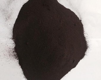 May include: A close-up of a pile of dark brown lac black powder on a white surface. The powder is finely ground and has a smooth texture.