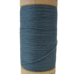 Puede incluir: Una bobina de hilo azul hecha de algodón orgánico 100%. La bobina es de madera y tiene el texto "100% ORGANIC COTTON" impreso en la parte superior y "MADE IN G" impreso en la parte inferior.