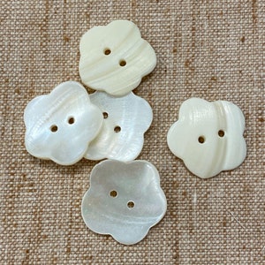 May include: Five white, pearl-like buttons in the shape of a flower with five petals. The buttons have two holes each.