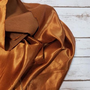May include: A close-up of a crumpled piece of fabric in a rich, golden brown color. The fabric has a subtle sheen and a smooth, silky texture.