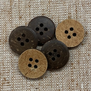 May include: Five brown and beige coconut shell buttons with four holes each. The buttons have a natural, rustic look.