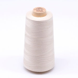 Könnte beinhalten: Eine Spule weißen Bio-Baumwollgarns mit einem Holzetikett mit der Aufschrift "I am organic - 100% cotton - 3000 yds - 50 wt - col 4899"