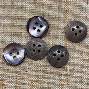 May include: Five brown shell buttons with four holes each. The buttons are arranged in a semi-circle on a beige fabric background.