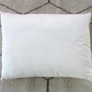 May include: A white pillow with a smooth, cotton-like texture. The pillow is lying flat on a gray and white patterned surface.