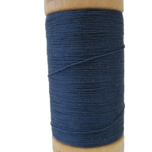 Puede incluir: Una bobina de hilo de algodón orgánico 100% azul oscuro en una bobina de madera. La bobina está etiquetada con "100% algodón orgánico" y "100m".