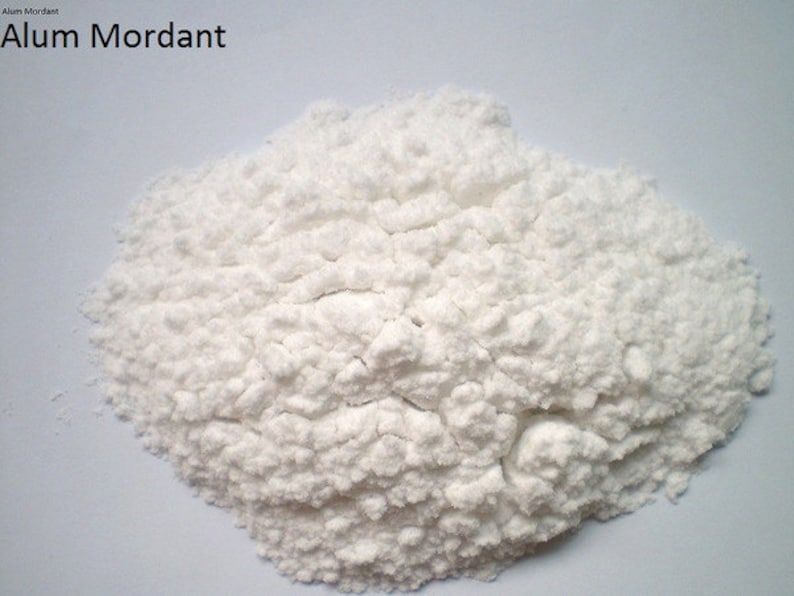 May include: A close-up of a pile of white alum mordant powder. Alum mordant is used in dyeing and printing to help dye adhere to fabric.